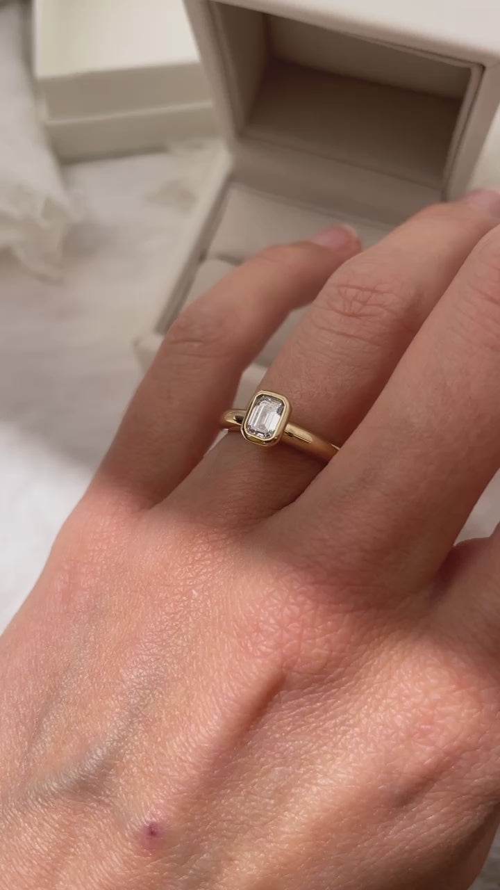 Load video: Emerald Cut Diamond bezel set Solitaire ring, cast in solid Gold. Handcrafted to order in Sydney Australia. Minimal Diamond Engagement ring ideal for stacking with other bands. Custom engagement and wedding rings.